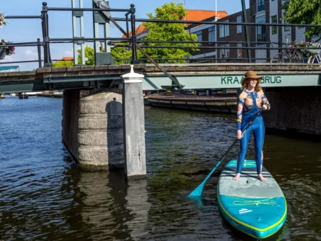 Vrouw met hoed peddelt op een supboard onder een brug door in de binnenstad van Leiden