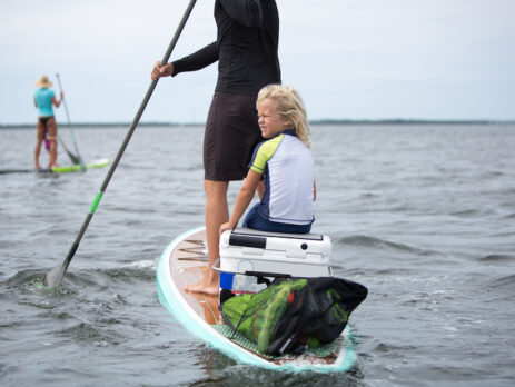 Jongetje zittend op een supboard achterop bij een peddelende vrouw